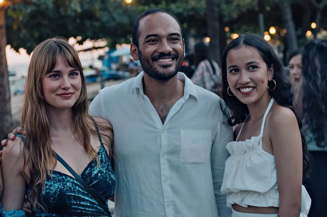 Three friends smiling and posing together at an outdoor evening event