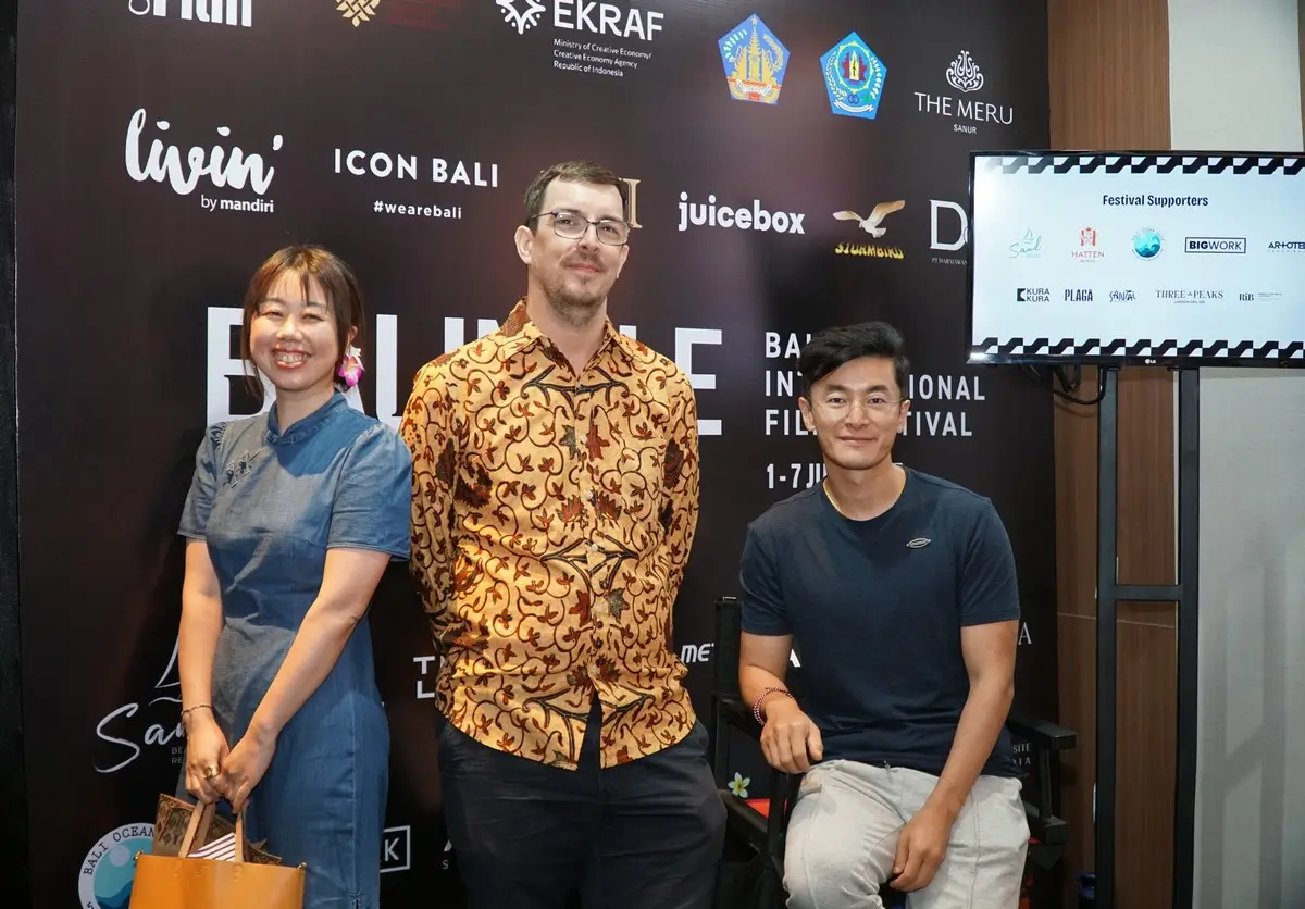 Three people posing in front of a press backdrop for the Bali International Film Festival